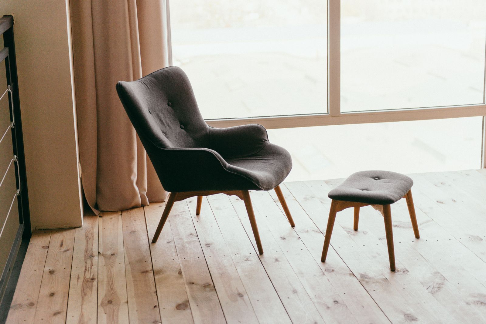 Fauteuil sombre et repose-pieds devant une grande fenêtre